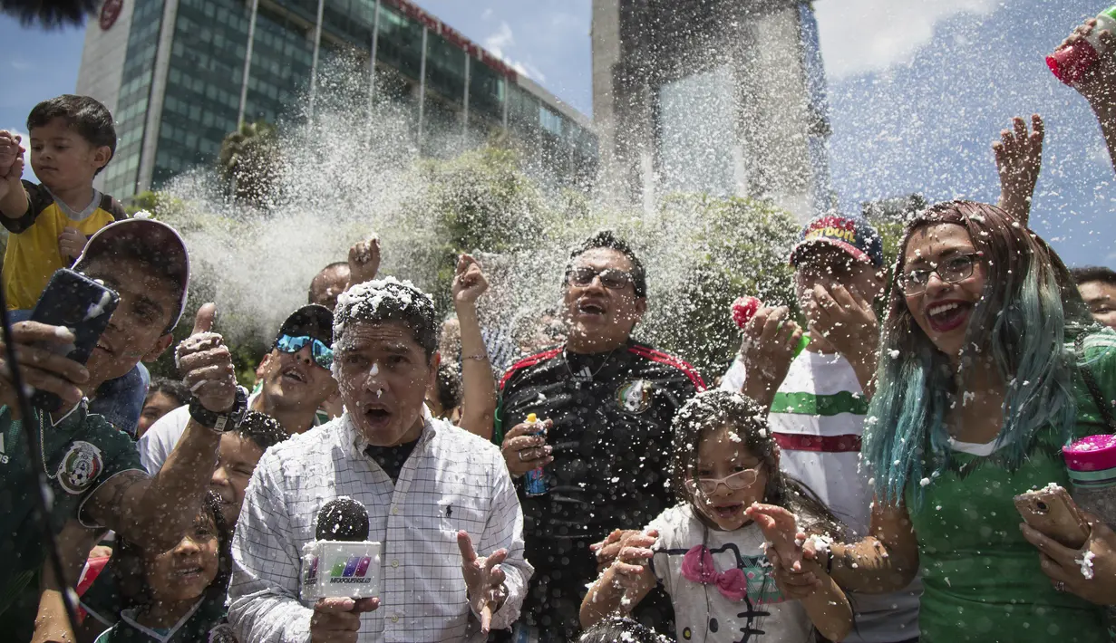 Seorang reporter ikut terkena semprotan busa saat fans Meksiko merayakan kemenangan timnya atas Jerman di Monumen Angel of Independence,  Meksiko City (17/6/2018). Meksiko menang 1-0. (AP/Anthony Vazquez)