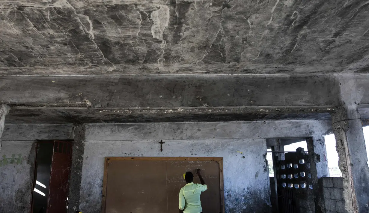 Seorang guru menulis di papan tulis selama kelas di sekolah Sante Bernadette, di dalam Fort Dimanche, yang pernah menjadi penjara di Port-au-Prince, Haiti, Kamis (23/9/2021). Minggu ini tahun ajaran dimulai di Haiti. (AP Photo/Rodrigo Abd)