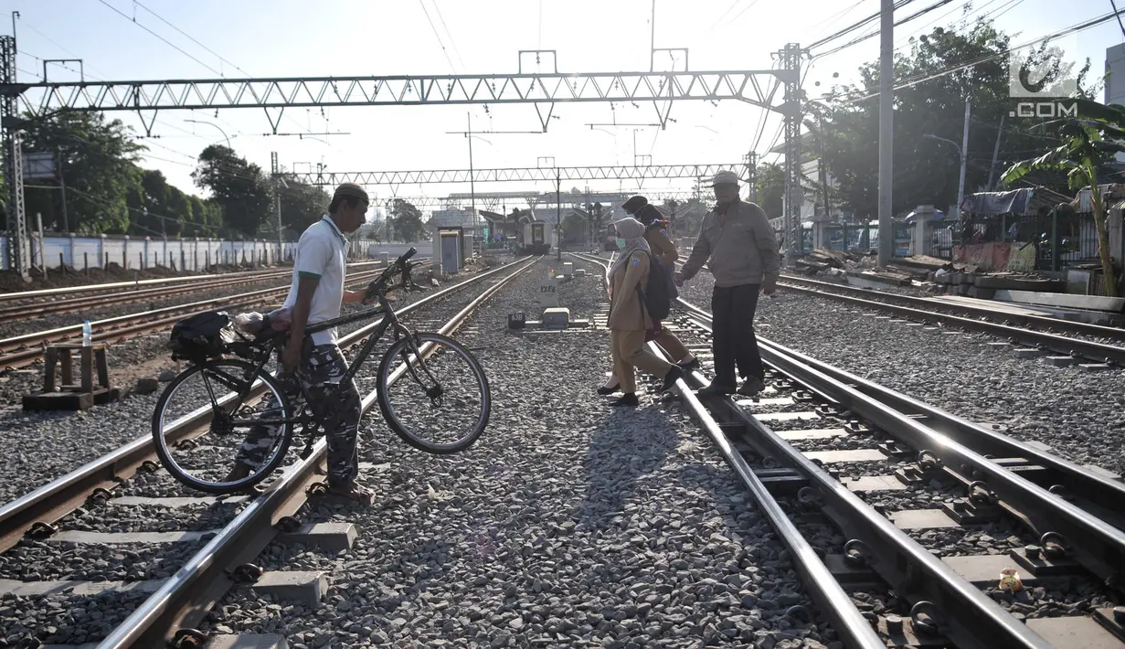 Seorang pria mengangkat sepedanya menyeberangi perlintasan rel kereta api di kawasan Pisangan Baru, Jakarta, Selasa (10/9/2019). Warga nekat menantang maut menyeberangi rel dekat stasiun Jatinegara tersebut lantaran tidak adanya akses jembatan penyeberangan orang (JPO). (merdeka.com/Iqbal Nugroho)