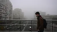 Seorang pria yang memakai masker melintasi jalan layang pada hari yang berkabut dan tercemar di Beijing, Sabtu (6/11/2021). Jalan raya dan taman bermain sekolah di Beijing ditutup pada Jumat (5/11) karena polusi kabut asap yang tebal, setelah China meningkatkan produksi batu bara. (JADE GAO/AFP)