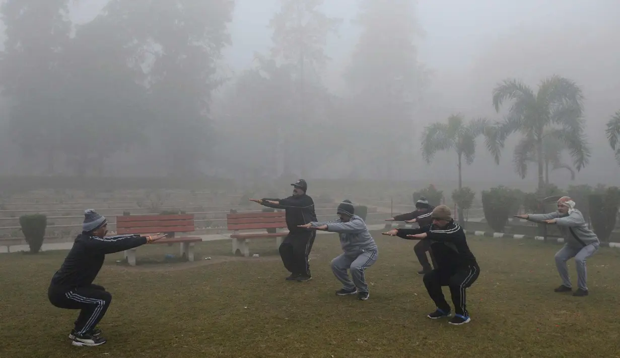 Sejumlah pria melakukan pemanasan saat berolahraga di tengah kabut tebal dan polusi udara di Amritsar, India (2/1). (AFP Photo/Narinder Nanu)
