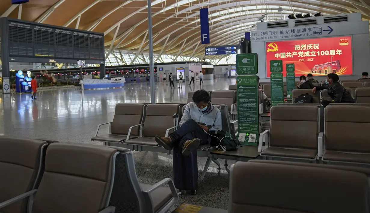 Penumpang beristirahat di dekat papan informasi penerbangan kosong di Bandara Internasional Pudong, Shanghai, Minggu (25/7/2021). China telah menutup jalur kereta api dan pelabuhan, serta membatalkan jadwal penerbangan sebelum topan In-Fa diperkirakan mendarat. (AP Photo/Andy Wong)