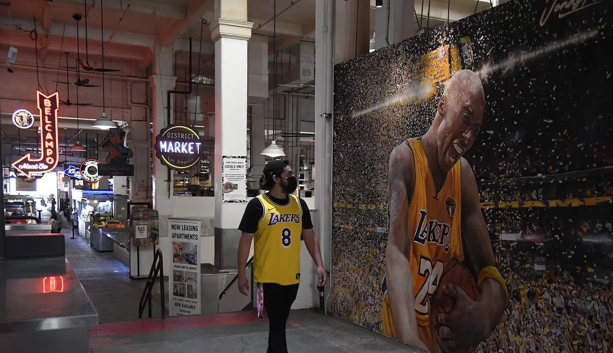 Seorang fans melintas di depan lukisan mural bintang LA Lakers, Kobe Bryant di Grand Central Market, Los Angeles, California, Selasa (26/1/2021). Lukisan dibuat untuk mengenang 1 tahun tragedi kecelakaan helikopter yang menewaskan Kobe Bryant dan putrinya, Gianna. (Getty Images via AFP/Sarah Stier)