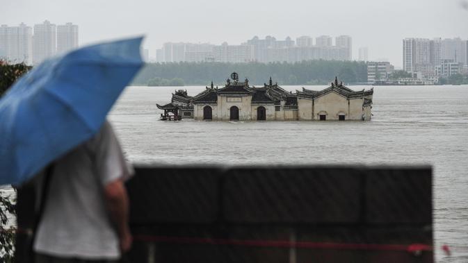 Warga memandangi kuil Guanyinge berumur 700 tahun yang dibangun di atas batu, terendam banjir akibat meluapnya sungai Yangtze di Wuhan, provinsi Hubei pada 19 Juli 2020. Hujan lebat sejak bulan Juni telah menyebabkan sedikitnya 141 orang tewas dan memaksa hampir 15 juta orang dievakuasi. (STR/AFP)