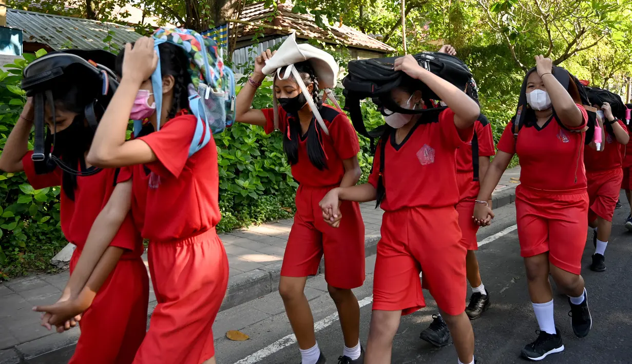 Anak-anak sekolah menggunakan tas mereka untuk melindungi diri saat latihan gempa dan tsunami di Tanjung Benoa, Kabupaten Badung, Bali, 24 Mei 2022. (SONY TUMBELAKA/AFP)