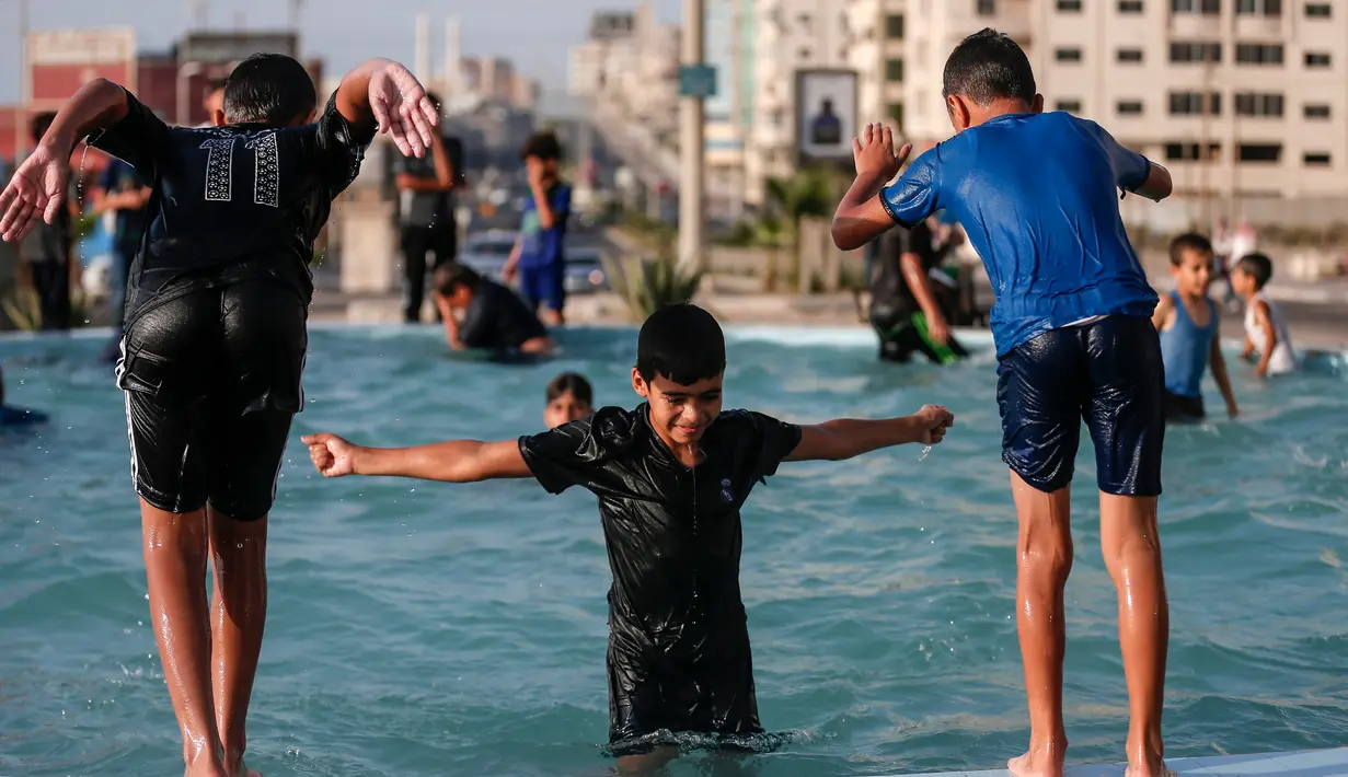 Anak-anak Palestina bermain di air mancur umum selama hari musim panas di Kota Gaza (20/7/2020). Musim panas yang terjadi di Palestina membuat anak-anak memenuhi air mancur. Mereka berupaya mendinginkan tubuh mereka dengan cara berenang di air mancur tersebut. (AFP Photo/Mahmud Hams)