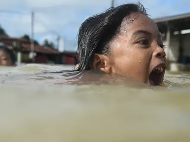Anak-anak berenang saat banjir melanda kawasan Rantau Panjang, Malaysia, Kamis (5/1). Sekitar 23 ribu orang terpaksa mengungsi karena banjir yang disebabkan hujan muson ini. (AFP PHOTO / MOHD RASFAN)