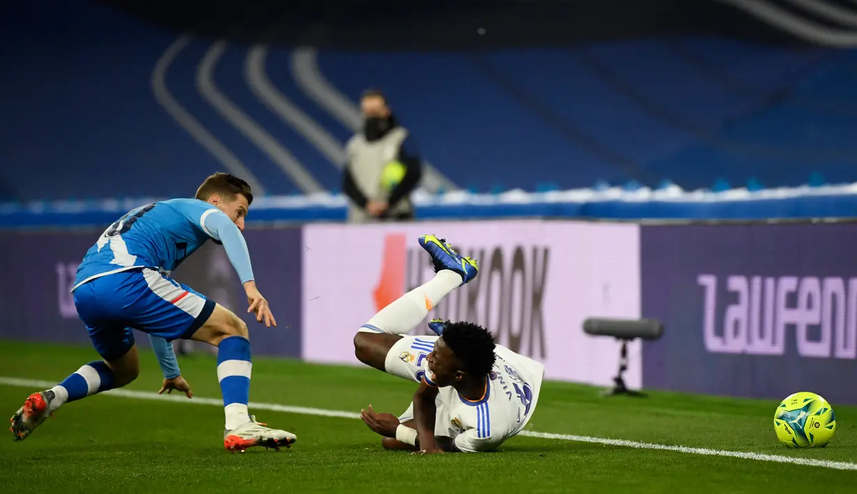 Penyerang Real Madrid Vinicius Junior jatuh saat bersaing dengan bek Rayo Vallecano, Ivan Balliu pada pekan ke-13 Liga Spanyol 2021/22 di Santiago Bernabeu, Minggu (7/11/2021) dini hari WIB. Real Madrid berhasil mengantongi tiga poin setelah menekuk Rayo Vallecano 2-1. (PIERRE-PHILIPPE MARCOU / AFP)