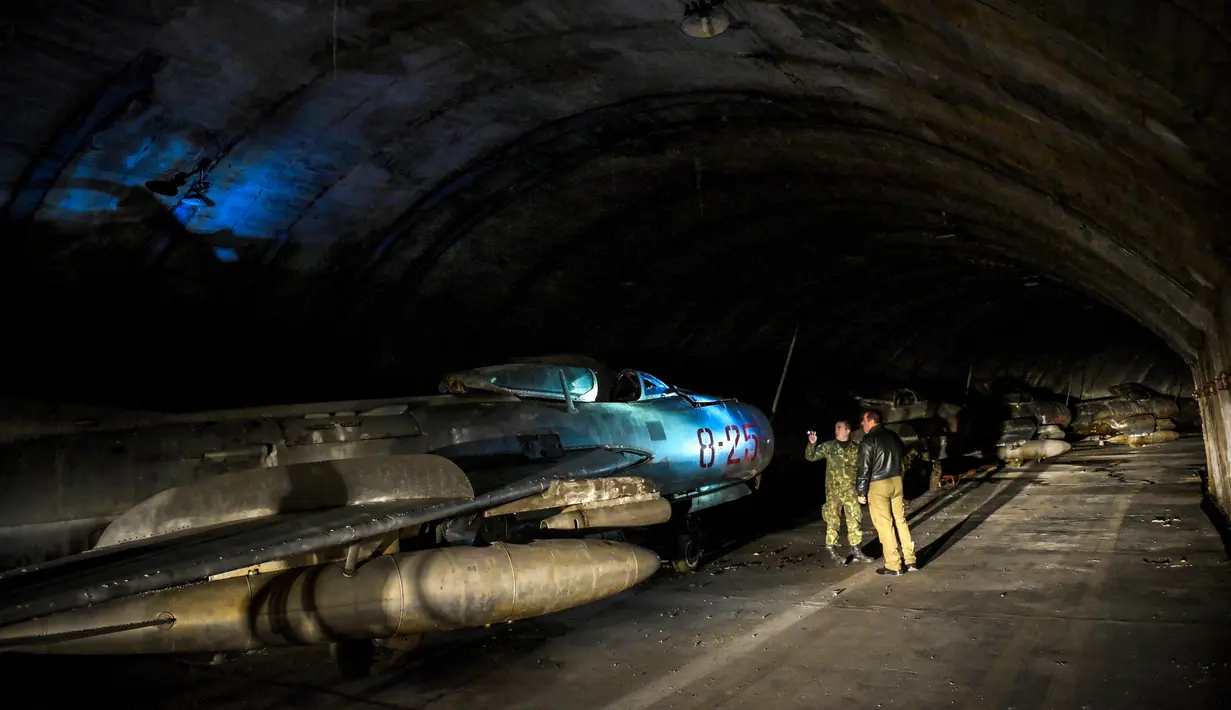 Tentara Albania berjalan di sebelah pesawat tempur MIG-19 dalam terowongan utama Pangkalan Udara Gjader di dekat Kota Lezhe, 5 Februari 2019. Pangkalan Udara Gjader berlokasi dalam perut gunung tandus. (Gent Shkullaku/AFP)