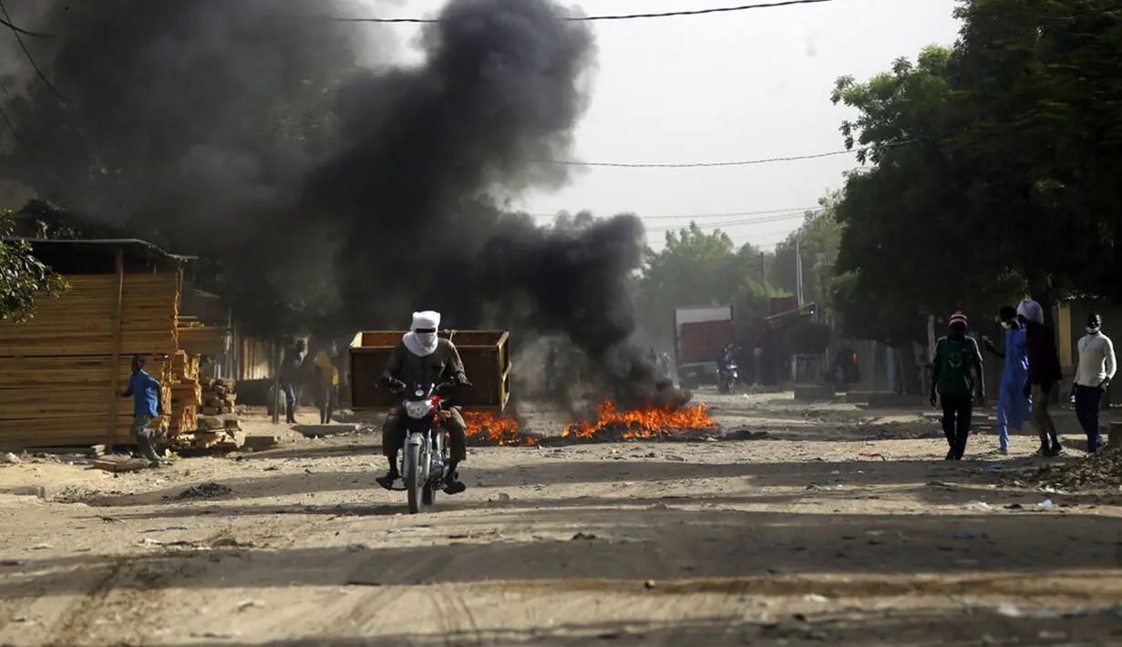 Seorang pria mengendarai sepeda motor melewati api menyusul protes di N'Djamena, Chad, Selasa (27/4/2021). Ribuan orang melakukan protes dan dua orang tewas dalam demonstrasi menentang aturan dewan militer transisi yang dipimpin putra Presiden Idriss Deby Itno yang terbunuh. (AP Photo/Sunday Alamba)