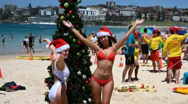 Turis memakai topi Santa foto di sebelah pohon Natal selama Hari Natal di Pantai Bondi di Sydney, Australia (25/12). (AFP Photo/Peter Parks)