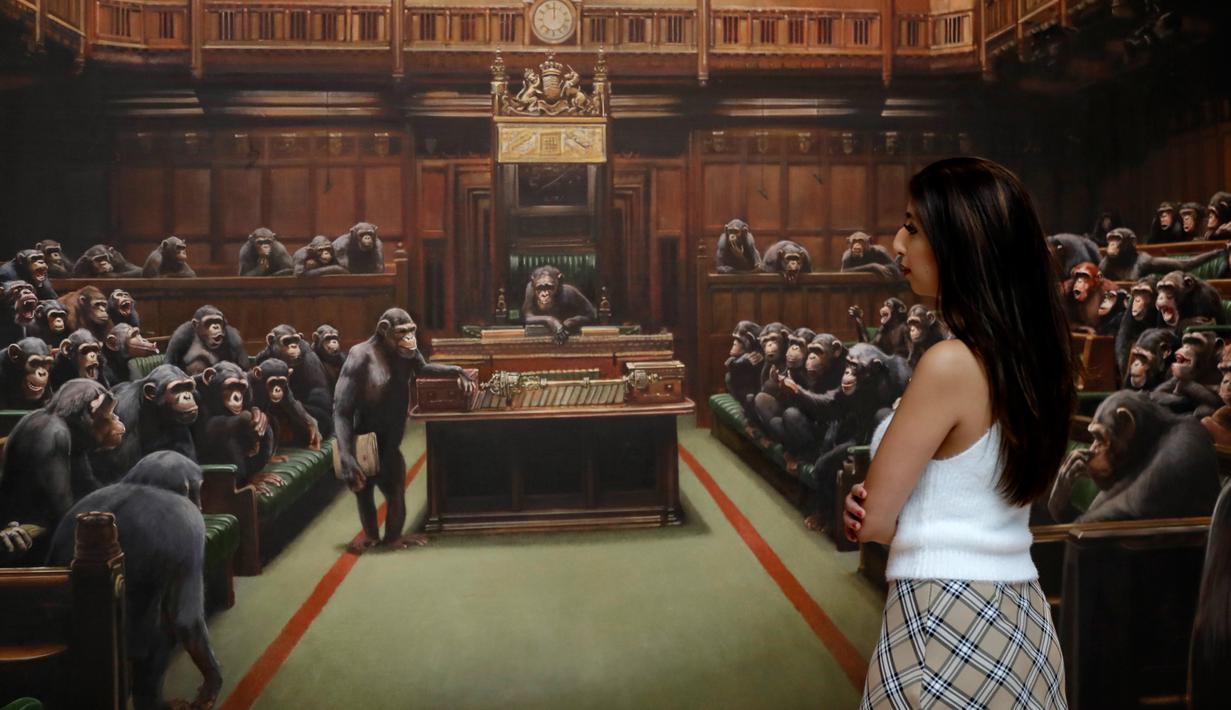 Petugas mengamati lukisan seniman jalanan Banksy yang dipajang di ruang lelang Sotheby, London, Jumat (27/9/2019). Karya Banksy tersebut dipuji publik karena relevan dengan situasi di tengah kekacauan Brexit yang dialami Inggris. (AP/Kirsty Wigglesworth)