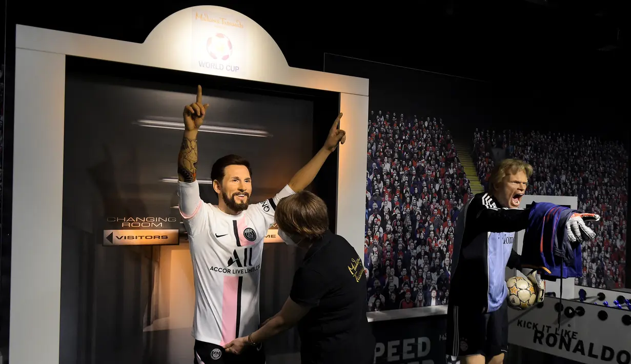 Seorang tim potret museum lilin Madame Tussauds Berlin, Karen Fries (kanan) memperbaiki jersey baru Paris Saint-Germain (PSG) pada patung lilin Lionel Messi di Berlin. (11/7/2021). (AFP/Tobias Schwarz)