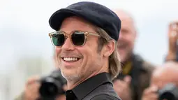 Aktor Brad Pitt tersenyum saat tiba menghadiri pemutaran film 'Once Upon a Time in Hollywood' selama Festival Film Cannes Internasional ke-72 di Prancis (22/5/2019).  Brad Pitt tampil santai mengenakan jeans hitam, kemeja polo hitam, kaca mata dan topi. (AP Photo/Joel C Ryan)
