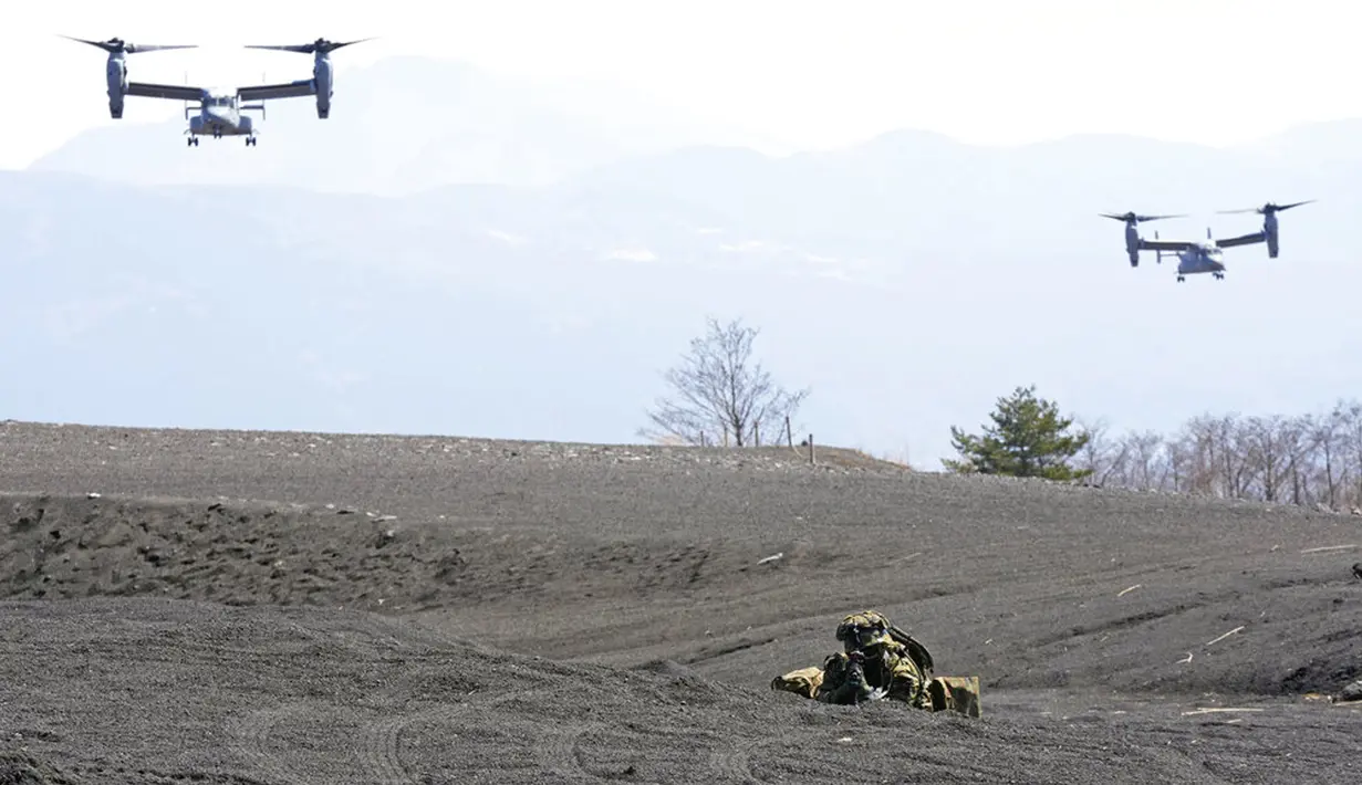 Dua MV-22 Ospreys terbang saat salah satu anggota Pasukan Bela Diri Darat Jepang (JGSDF) menjaga zona pendaratan pada latihan militer gabungan antara JGSDF dan Marinir AS di Higashi Fuji, Gotemba, Jepang, Selasa (15/3/2022). (AP Photo/Eugene Hoshiko)