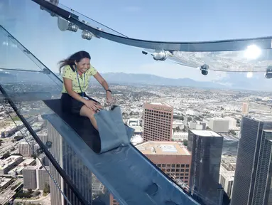 Seorang wanita mencoba berseluncur menggunakan skyslide di lantai 69 dan 70 dari Bank Tower AS, Los Angeles , California, (20/6). Tempat yang dinamakan OUE Skyspace LA ini kita dapat melihat panorama indah kota LA dari atas. (REUTERS / Lucy Nicholson)