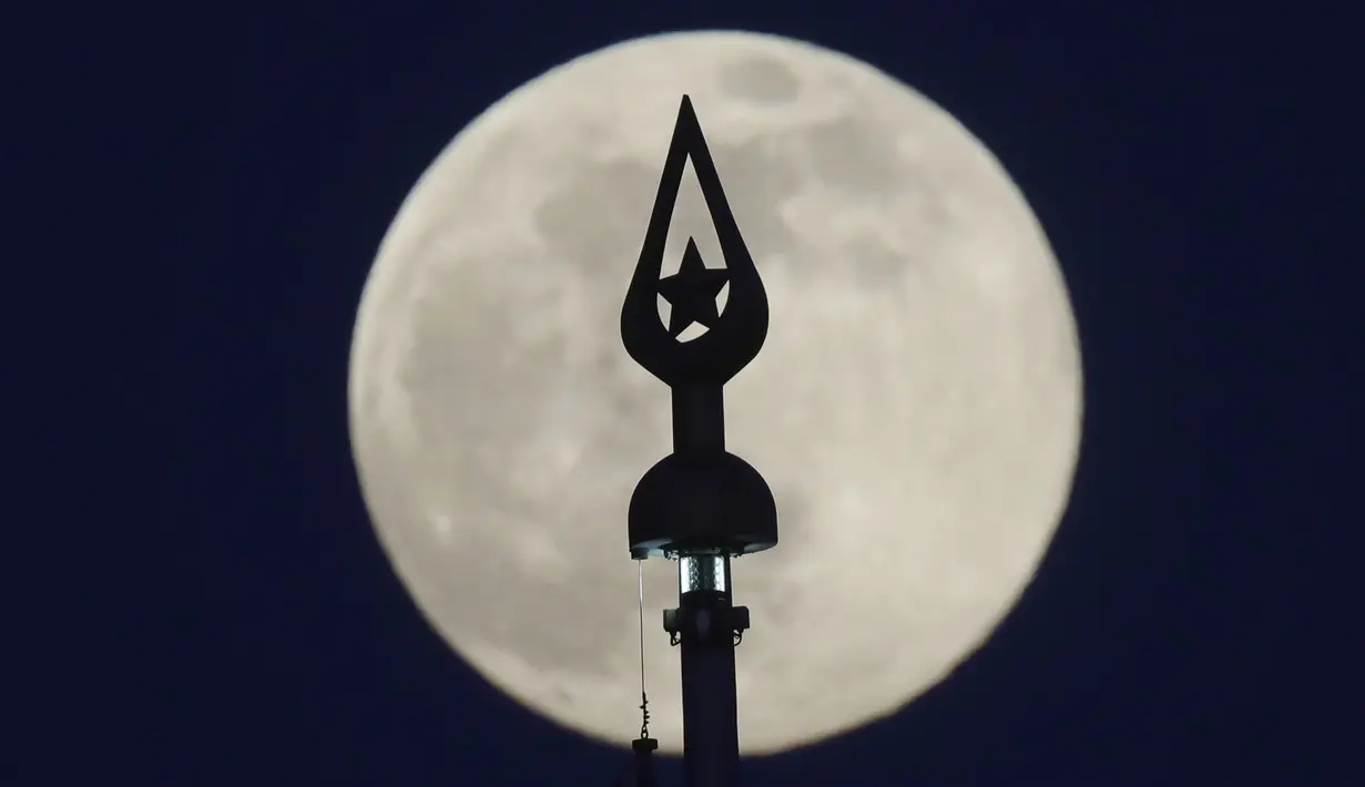 Supermoon terlihat di belakang tiang bendera di State Flag Square di Minsk, Belarus, Selasa (7/4/2020). Fenomena dimana bulan berada pada titik terdekat dengan bumi ini merupakan penampakan supermoon terbesar di tahun 2020. (AP Photo/Sergei Grits)