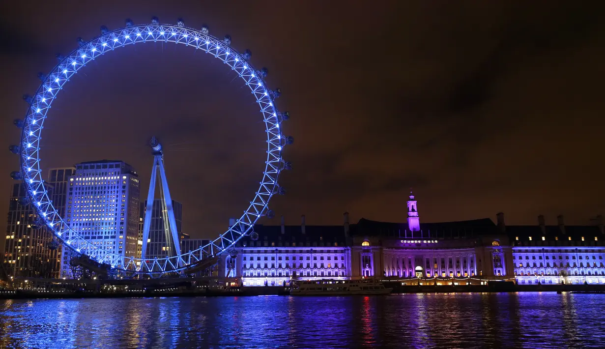 London Eye di tepi Sungai Thames diterangi dengan lampu biru untuk berterima kasih kepada National Health Service (NHS) di London, Kamis (7/1/2021). NHS merupakan sistem layanan kesehatan nasional yang menjadi ujung tombak Inggris dalam memerangi pandemi Covid-19. (AP Photo/Kirsty Wigglesworth)