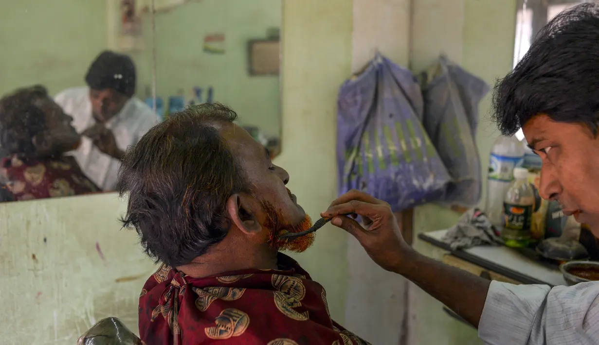 Dalam gambar yang diambil pada 19 Januari 2019, tukang cukur Mohammad Shadat Hossain mewarnai janggut pelanggannya dengan pacar (henna) di Dhaka. Penampilan ini didorong juga dengan kepercayaan terhadap tulisan-tulisan agama yang mengatakan Nabi Muhammad mengecat rambutnya. (MUNIR UZ ZAMAN / AFP)