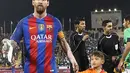 Bintang Barcelona Lionel Messi berjalan sambil menggandeng bocah Afghanistan, Murtaza Ahmadi (kanan) saat memasuki lapangan sebelum pertandingan persahabatan melawan Al-Ahli di ibu kota Qatar, Doha, Selasa (13/12). (Karim Jaafar/AFP)