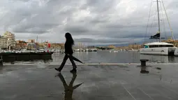 Seorang wanita berjalan dengan payungnya di Vieux-Port di Marseille, Prancis selatan,  Senin (4/10/2021). Wilayah Prancis selatan dalam siaga untuk hujan lebat dan banjir. (AFP Photo/Nicolas Tucat)