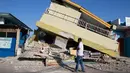 Seorang pria berjalan melewati bangunan yang runtuh akibat gempa di Reo, provinsi Nusa Tenggara Timur, Indonesia, Senin, 17 Agustus 2026. (AP Photo/Firdia Lisnawati)