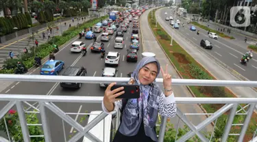 Seorang pejalan kaki berswafoto di jembatan penyeberangan orang (JPO) yang tidak beratap di jalan Sudirman, Jakarta, Rabu (6/11/2019). Pemprov DKI mengklaim mayoritas masyarakat Jakarta setuju dengan konsep JPO terbuka dan tanpa atap yang kini dibangun di Sudirman. (merdeka.com/Arie Basuki)