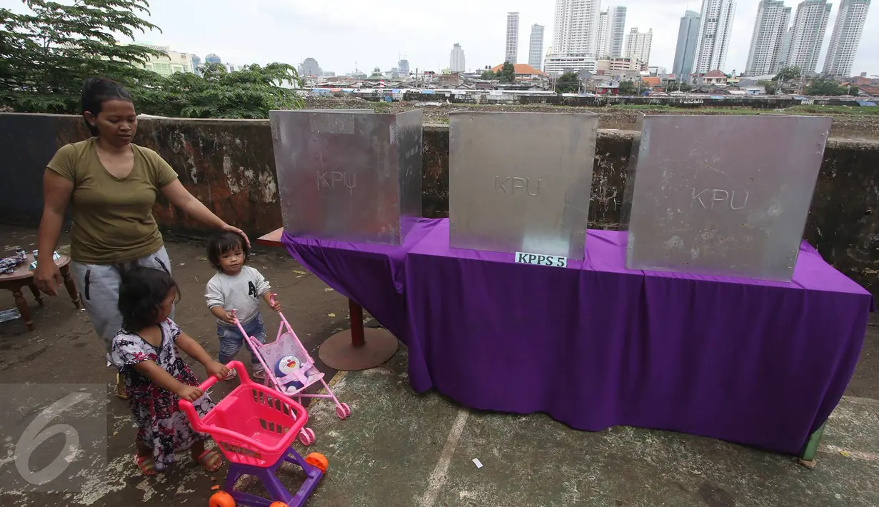 Seorang wanita bersama dua orang bocah melintas di dekat bilik suara di TPS 023 Petamburan, Jakarta, Rabu (15/2). Di kawasan itu, petugas melakukan jemput suara kepada warga lansia yang tidak sanggup berjalan menuju TPS (Liputan6.com/Immanuel Antonius)