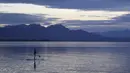 Seorang wanita muda mengontrol papan dayung, di danau Chiemsee saat matahari terbenam di Chieming, Jerman, Selasa, (25/8/2020). (AP Photo / Matthias Schrader)