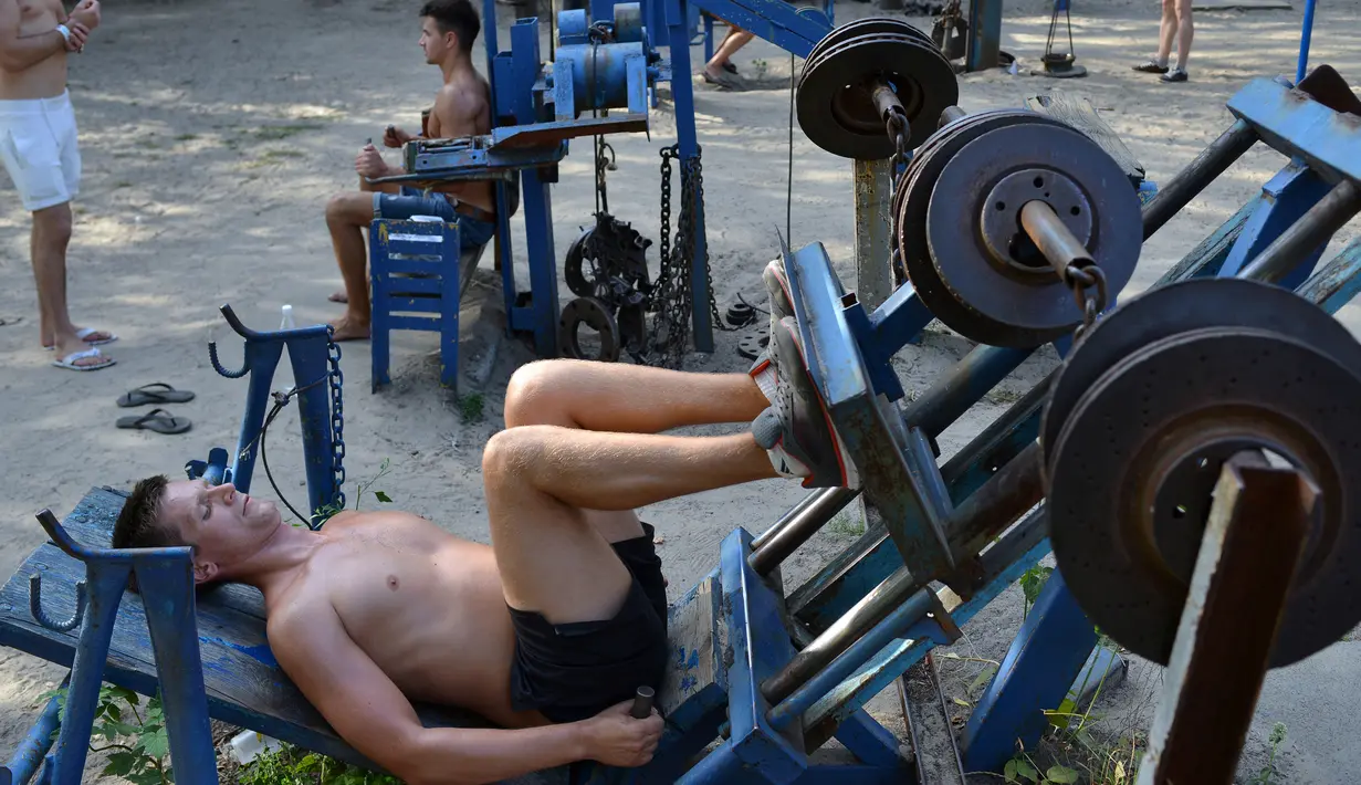 Seorang pria mendorong sebuah alat berat menggunakan kakinya di sebuah gym outdoor di Ibu Kota Ukraina, Kiev, 18 Agustus 2017. Alat olahraga di taman Kachalka itu dibuat seorang teknisi bernama Yuri Kook pada dekade 1970-an. (GENYA SAVILOV/AFP)