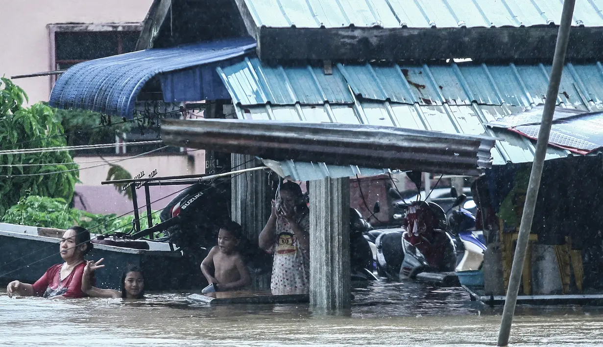Warga dan anak-anak berada di depan rumah yang terendam banjir di Rantau Panjang, timur laut Malaysia, Selasa (3/1). Akibat hujan lebat yang turun terus menerus selama empat hari di Malaysia, 5.000 warga terpaksa dievakuasi. (AFP PHOTO/STR/Malaysia OUT)