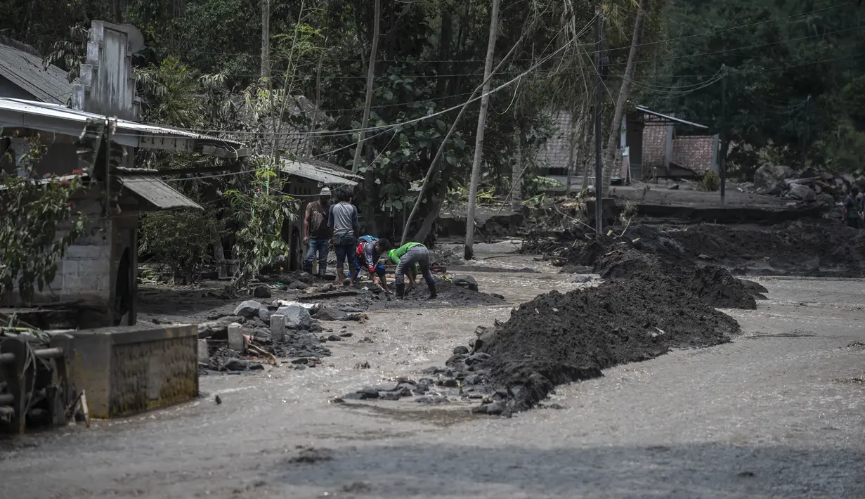 Warga membersihkan abu dan lumpur di sekitar rumah yang rusak di Dusun Kamar Kajang, Lumajang, Kamis (9/12/2021). Luapan air sungai bercampur material lahar dingin erupsi Gunung Semeru merendam puluhan rumah akibat diguyur hujan deras pada Selasa (7/12) dan Rabu (8/12) malam. (Juni Kriswanto/AFP)