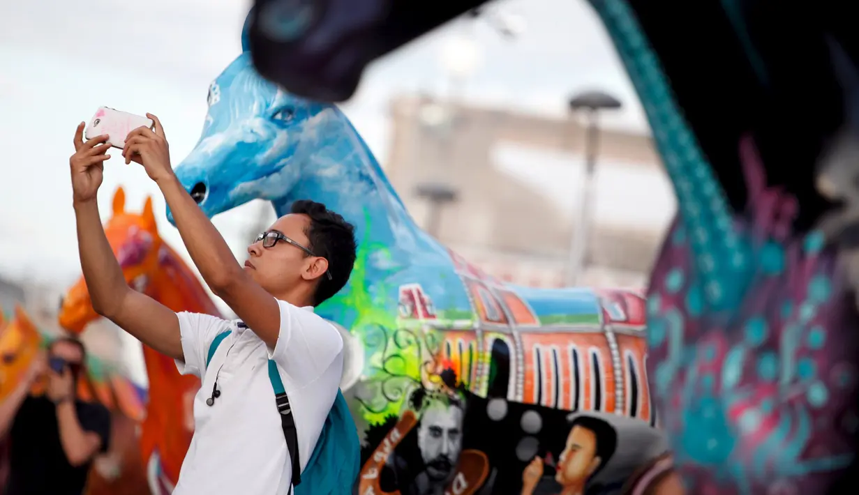 Seorang Pria berselfie dengan patung kuda di pusat kota Ciudad Juarez, Meksiko, Selasa (25/8/2015). Kuda – kuda ini dibuat dan dilukis oleh para seniman lokal Meksiko. (REUTERS/Jose Luis Gonzalez)