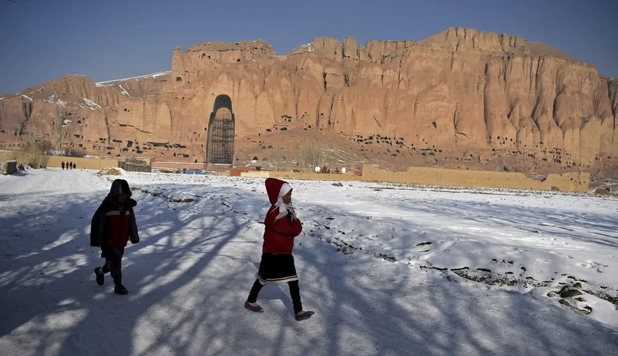 Anak-anak berjalan melalui jalan yang tertutup salju setelah turun salju dekat situs patung Buddha raksasa yang dihancurkan oleh Taliban pada 2001 di Provinsi Bamiyan, Afghanistan, 8 Januari 2021. Dahulu, daerah patung ini berdiri juga menjadi rumah untuk biara. (WAKIL KOHSAR/AFP)