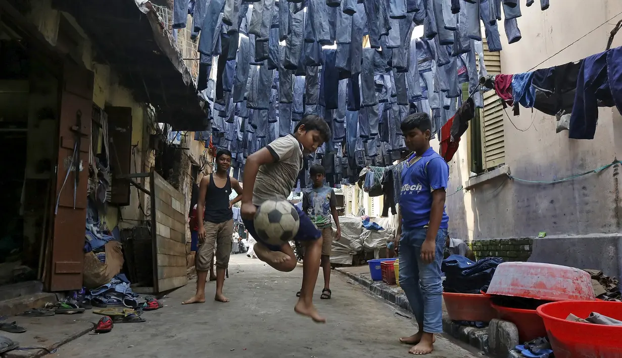 Anak-anak bermain bola di sebuah gang dengan jeans tergantung untuk dijual di pasar pakaian bekas di Kolkata, India, 10 Maret 2016. Kota ini memiliki kekurangan perumahan yang parah, setidaknya 1 juta orang tidur di jalan. (REUTERS/Rupak De Chowdhuri)