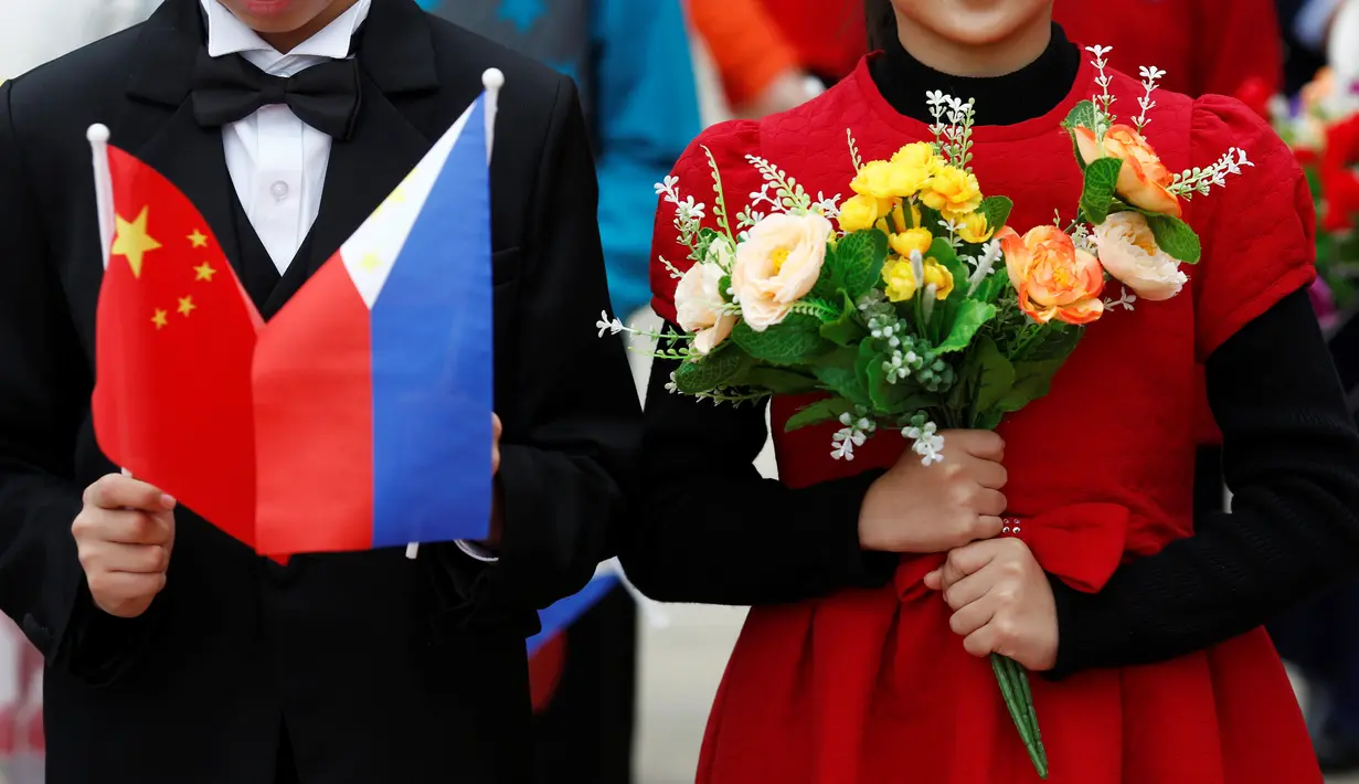 Sepasang anak-anak memegang bunga plastik dan bendera nasional Tiongkok dan Filipina pada saat menyambut kedatangan Presiden Filipina, Rodrigo Duterte di Balai Agung Rakyat Tiongkok, Beijing (20/10). (Reuters/Thomas Peter)