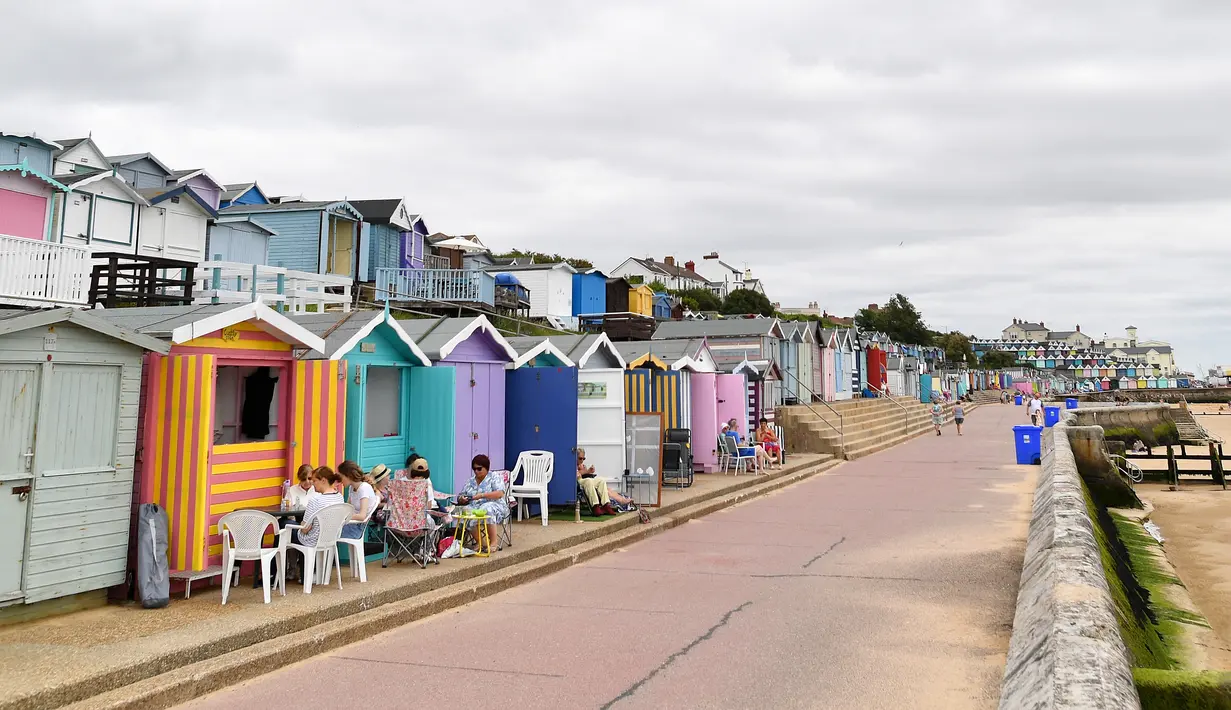 Orang-orang duduk di luar gubuk pantai di Walton-on-the-Naze, di Inggris pada 15 Juli 2021. Gubuk kayu yang dicat cerah berjajar di garis pantai Inggris telah menikmati booming selama pandemi, ketika orang-orang menemukan kembali tempat istirahat di tepi pantai di dekat rumah. (Justin TALLIS/AFP)
