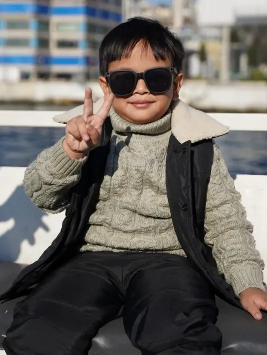 Tampil stylish dengan padu padan turtleneck sweater warna hijau army, vest hitam, dan long pants warna senada.