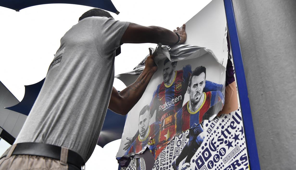 Seorang pekerja melepas poster-poster yang menampilkan pemain depan Barcelona Lionel Messi di stadion Camp Nou di Barcelona (10/8/2021). Prancis menunggu dengan tidak sabar Lionel Messi dengan para pendukung berkumpul di luar lapangan Paris Saint-Germain. (AFP/ Pau Barrena)