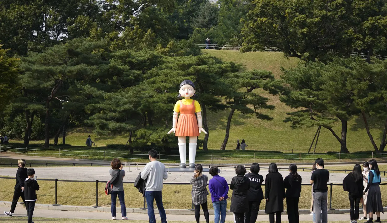 Pengunjung melihat boneka 'Younghee' yang menjadi maskot dalam serial Netflix asal Korea, Squid Game, di Olympic park, Seoul, Selasa (26/10/2021). Boneka setinggi empat meter atau 13 kaki itu, akan dipamerkan di taman tersebut selama tiga bulan. (AP Photo/Lee Jin-man)