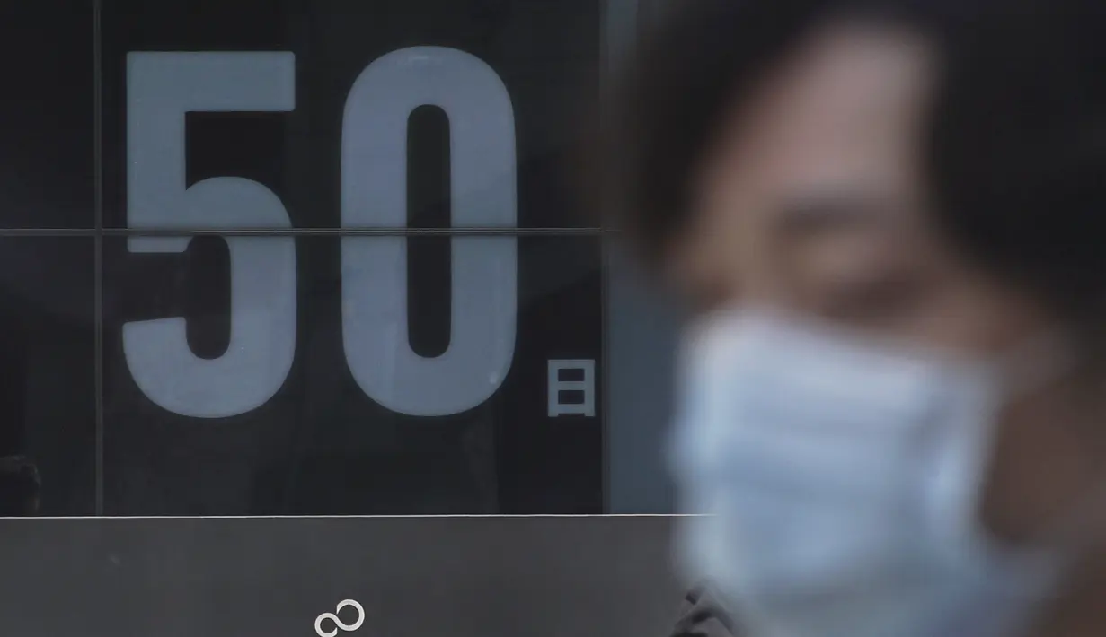Seorang pria berjalan melewati papan hitung mundur untuk Olimpiade Tokyo 2020 50 hari sebelum upacara pembukaan, di Tokyo, Kamis (3/6/2021). (AFP/ Kazuhiro Nogi)