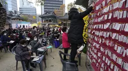 Seorang wanita menggantungkan kertas untuk mendoakan keberhasilan anaknya dalam ujian masuk perguruan tinggi di kuil Buddha Jogyesa, Seoul, Rabu (17/11/2021). Sekitar 500.000 siswa SMA di Korea Selatan diperkirakan akan mengikuti Tes Kemampuan Skolastik Perguruan Tinggi. (AP Photo/Ahn Young-joon)