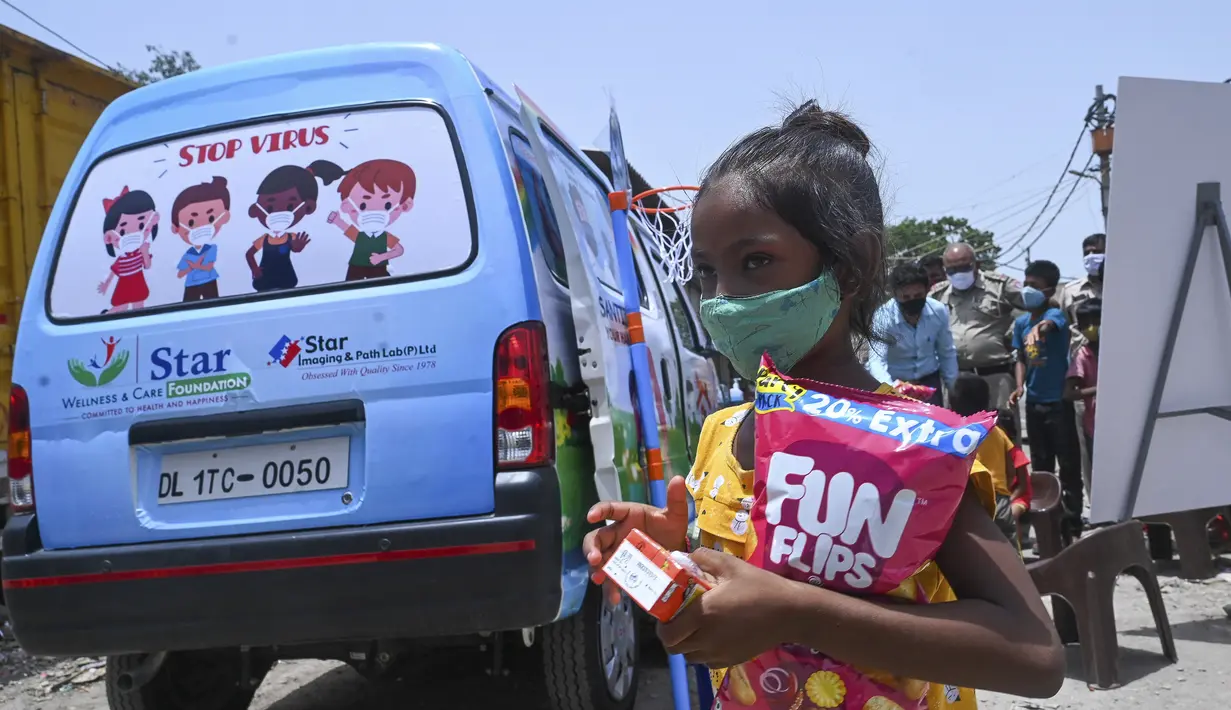 Seorang gadis pergi dengan makanan ringan setelah memberikan sampel swab untuk menguji virus corona Covid-19 di dalam sebuah van di New Delhi, India (1/7/2021).  Kegiatan ini diselenggarakan oleh Polisi Delhi bekerja sama dengan lab Star Imaging and Path. (AFP/Prakash Singh)