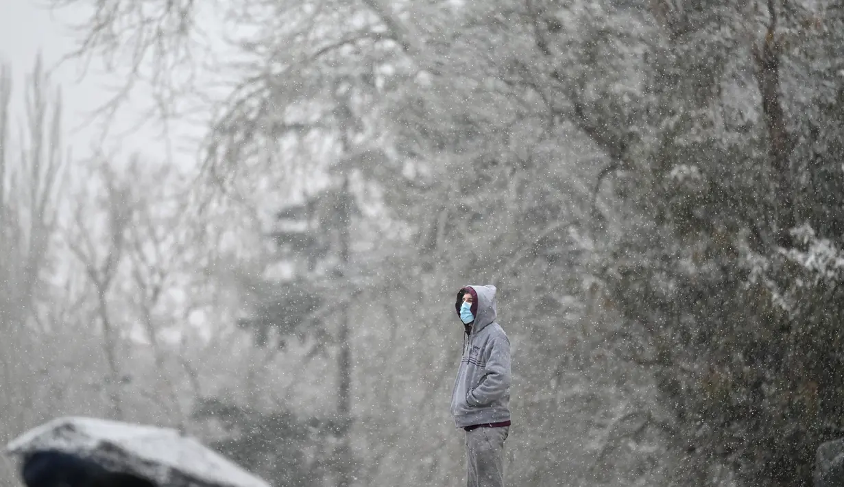 Seorang pria berdiri saat salju turun di Taman Retiro di pusat kota Madrid (7/1/2021). Wilayah timur Castilla-La Mancha, wilayah Madrid dapat melihat timbunan salju dengan total antara 20 dan 50 sentimeter. (AFP/Gabriel Bouys)