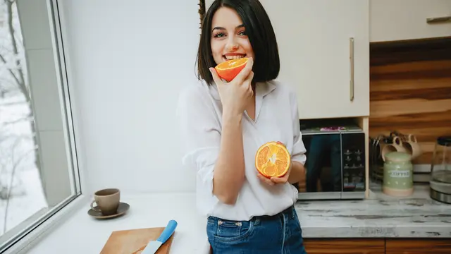 Seorang perempuan sedang memakan buah jeruk di dapur (Foto Dok: Freepik/prostooleh)