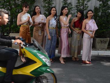 Pengendara motor melintas di depan sejumlah wanita yang mengenakan kostum tradisional setelah upacara agama Buddha sebagai persiapan untuk festival tahun baru Songkran di luar kantor di Bangkok, Thailand (9/4). (AFP Photo/Romeo Gacad)