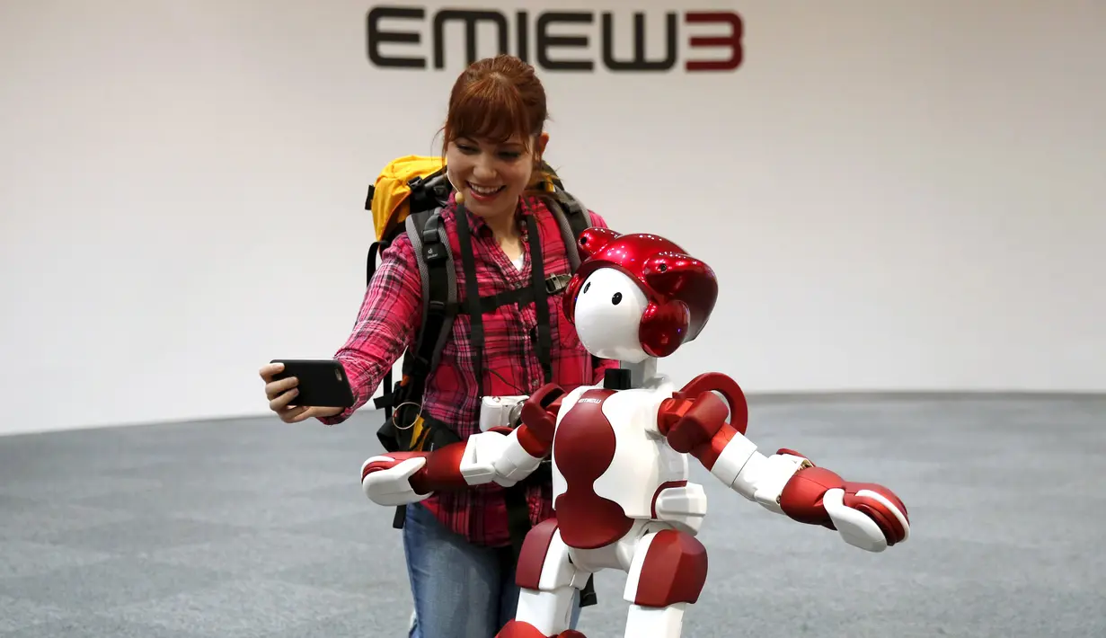 Petugas Hitachi Ltd berselfie dengan robot humanoid 'EMIEW 3' di Tokyo, Jepang, (8/4). Robot ini dikembangkan untuk memberikan layanan dan bimbingan yang diperlukan di toko-toko dan fasilitas umum. (REUTERS/Issei Kato)