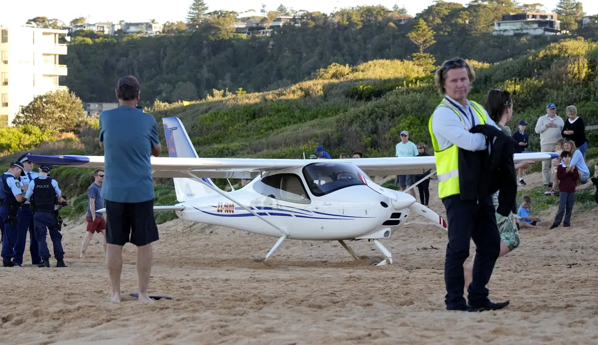Orang-orang berdiri di dekat sebuah pesawat ringan yang mendarat darurat di sebuah pantai di Sydney, Rabu (26/5/2021). Pesawat kategori rekreasi itu mendarat selamat di pantai Sydney dengan tiga orang di dalamnya termasuk seorang bayi setelah mengalami kerusakan mesin. (AP Photo/Mark Baker)