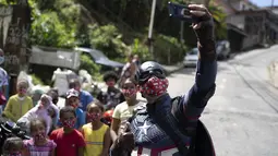 Polisi militer Everaldo Pinto, berkostum Captain America, berfoto dengan anak-anak di tengah pandemi COVID-19 di Petropolis, Rio de Janeiro, Brasil, Kamis (15/4/2021). Dalam aksinya, Pinto membagikan kotak berisi produk pembersih dan masker untuk mencegah paparan corona. (AP Photo/Silvia Izquierdo)