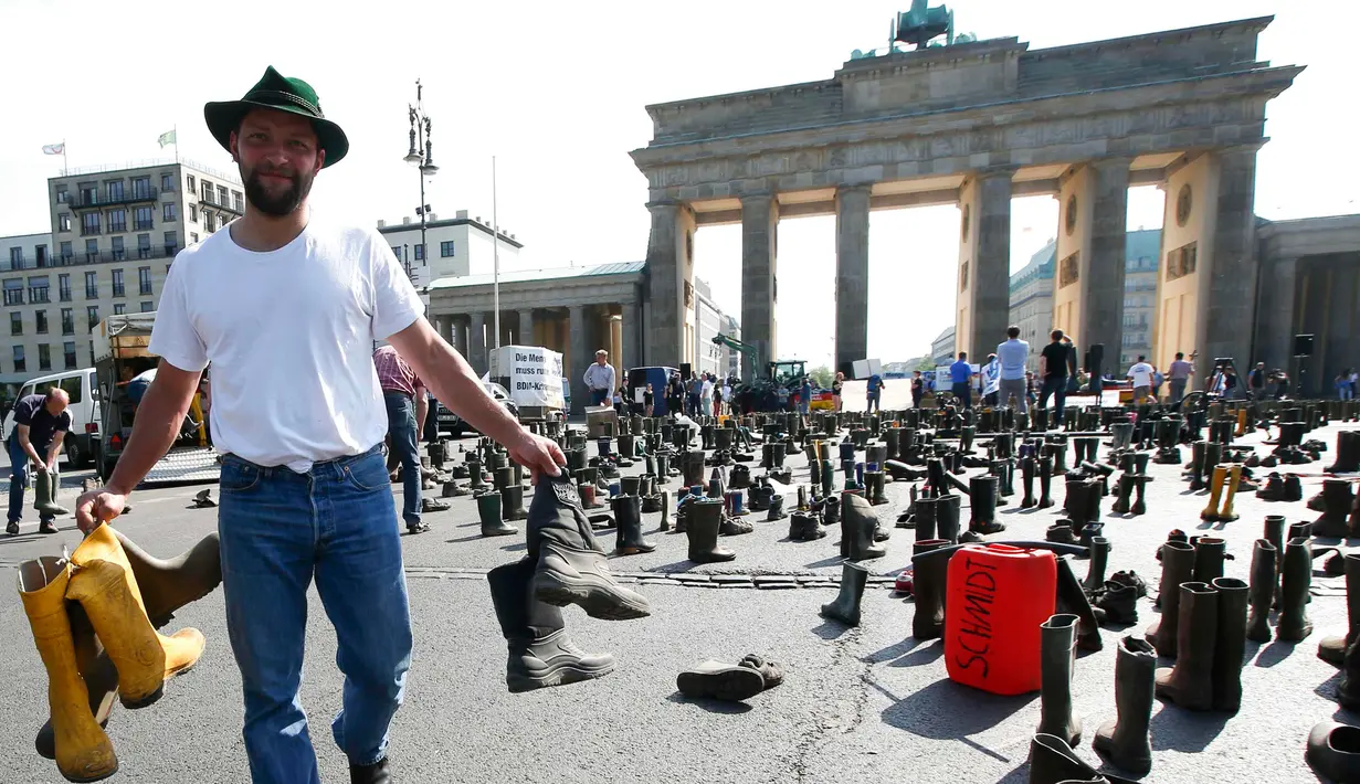 Seorang peternak sapi perah menyebarkan sepatu boots selama aksi protes di depan gerbang Brandenburg, Berlin, Jerman, Senin (30/5).  Mereka menuntut harga produk susu yang lebih adil bagi para peternak. (REUTERS/Fabrizio Bensch)